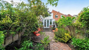 A garden pathway leading to a conservatory, surrounded by lush greenery and a wooden fence. - Beautiful Family Home w/ Parking in Central Oxford -Pass the Keys (Oxford)