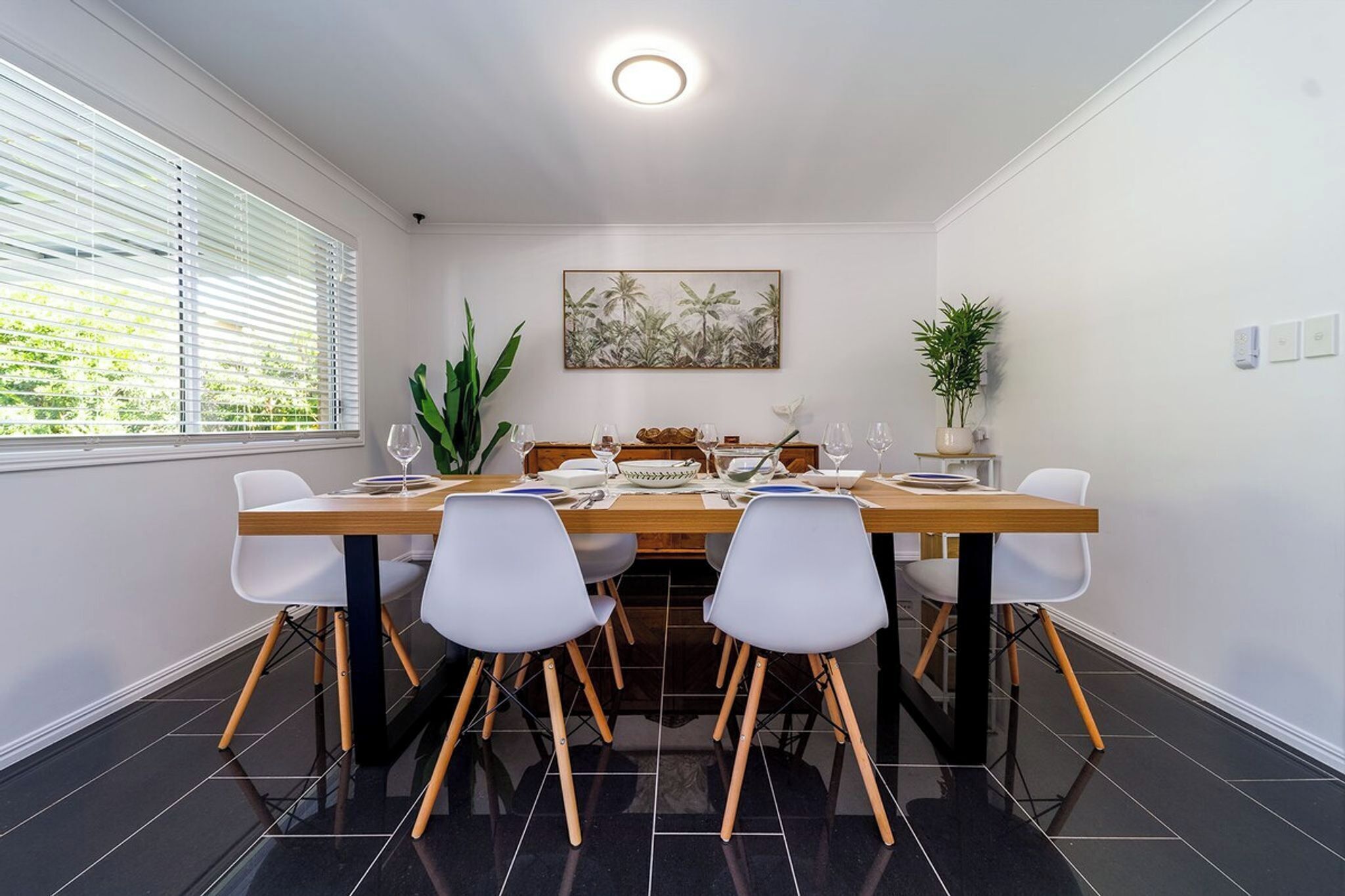 A dining area with a wooden table, white chairs, and a painting on the wall.