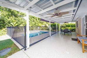 Un espace extérieur abrité comprenant une piscine, un ventilateur de plafond et une table de patio.