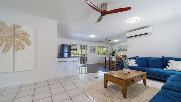 Ein modernes Wohnzimmer mit einem blauen Sofa, einem Holztisch und einem Deckenventilator.