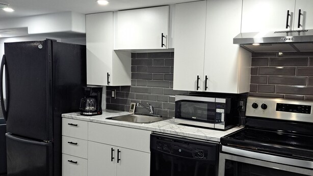 A modern kitchen with white cabinets, a black refrigerator, a microwave, a dishwasher, and a stainless steel stove. - Little cozy home (Belle River)