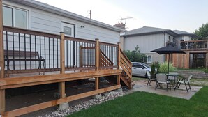 A deck with a wooden railing, a car parked in the driveway, and a patio area with outdoor furniture. - Little cozy home (Belle River)