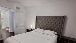 A bedroom with a large bed, a nightstand, a lamp, a door, and a ceiling light. - Little cozy home (Belle River)