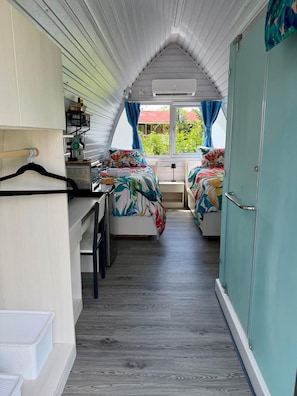 Une chambre de taille modeste, équipée de deux lits, d’un coin cuisine et d’une fenêtre avec des rideaux.