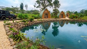 Un cadre extérieur paisible avec une piscine, deux cabanes en bois et un jeep garé à proximité.