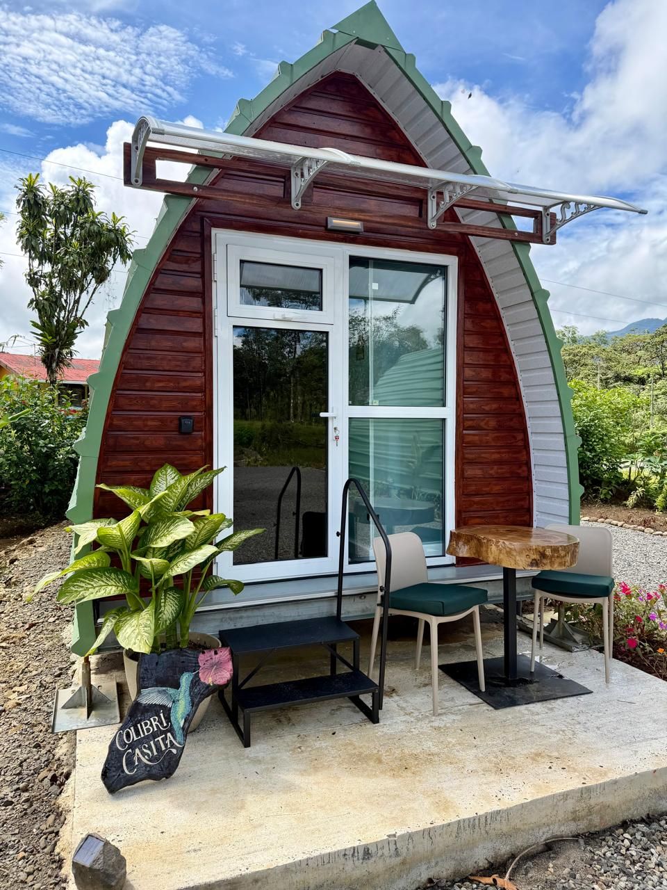 Ein kleines, rustikales Blockhaus mit Holzfassade, Glastür und einer Terrasse mit Tisch und Stühlen.