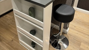 A modern kitchen with a black countertop, white storage shelves, a bar stool, and a vase with a red rose. - Suity-Centrum (Hamburg)
