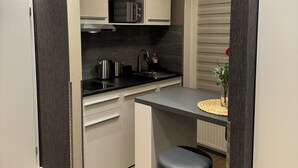 A compact kitchen with a microwave, sink, and bar stool, featuring dark wood paneling and a light-colored countertop. - Suity-Centrum (Hamburg)