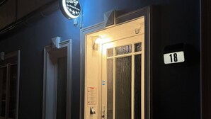 A building with a lit entrance door, a number sign '18', and a neon sign above the door. - Suity-Centrum (Hamburg)
