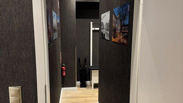 A hallway with dark walls, a wooden floor, and a door leading to a room. - Suity-Centrum (Hamburg)