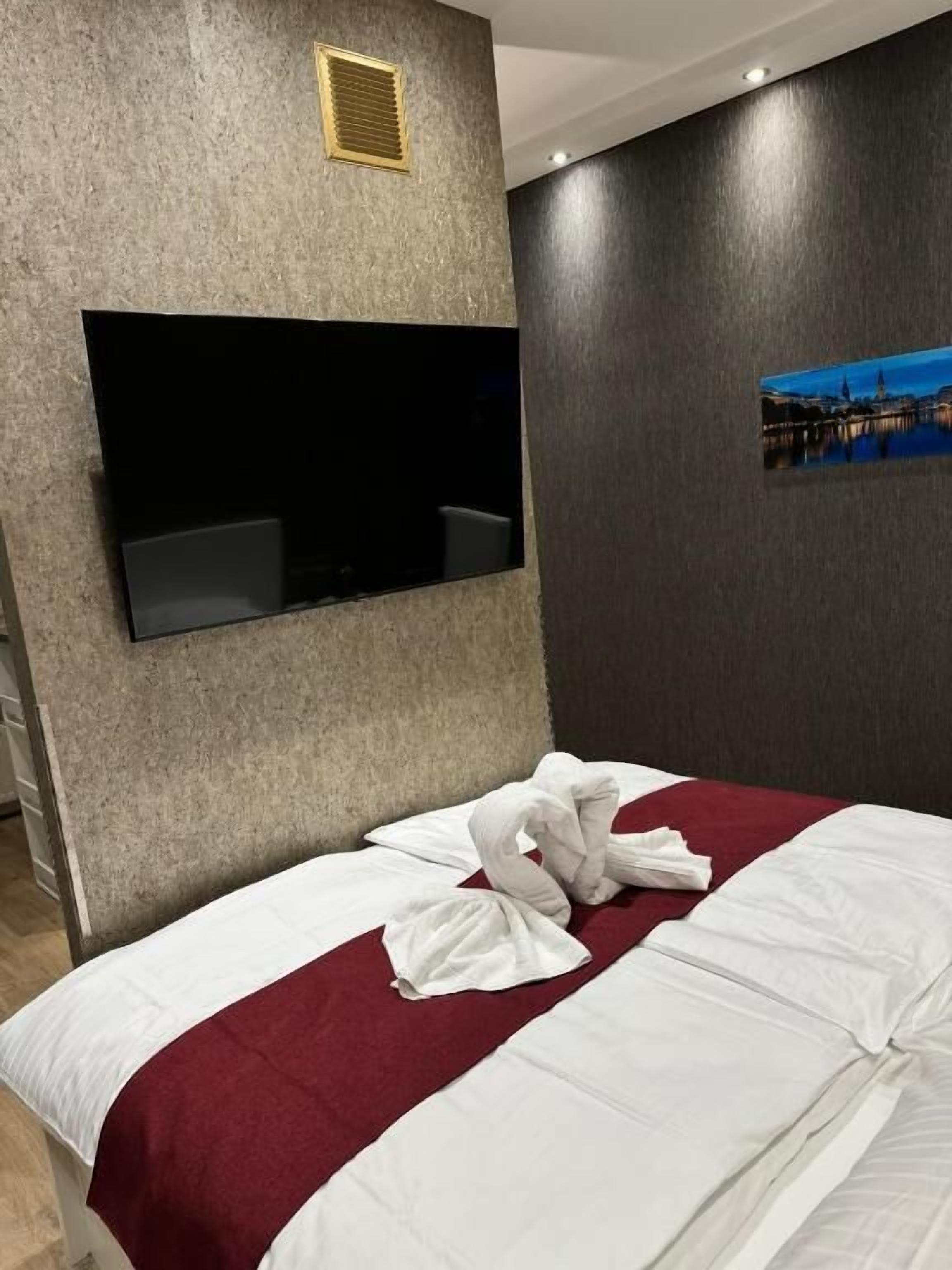 A hotel room with a bed, a mounted TV, a wall-mounted vent, and a framed picture.