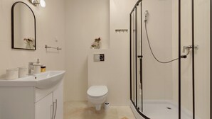 A modern bathroom with a white sink, toilet, and glass-enclosed shower. - Mostek 2101 PinkGray by Grand Apartments (Gdańsk)