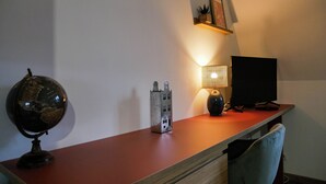 Un bureau avec un globe terrestre, une lampe et un écran d’ordinateur, dans une pièce dont le plafond est en pente et qui est dotée d’une étagère sur laquelle est posé un tableau.