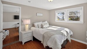 A bedroom with a bed, nightstand, lamp, and a window with a view. - Waterview Half-Duplex -Walk 2 Seagull Beach/Kayaks (Yarmouth)