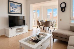 Ein Wohnzimmer mit Flachbildfernseher, Couchtisch, Sofa, Essbereich mit Stühlen und Stadtblick durch große Fenster.