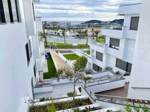 Ein modernes Mehrfamilienhaus mit Balkonen, einem Swimmingpool und Blick auf die Stadtlandschaft.