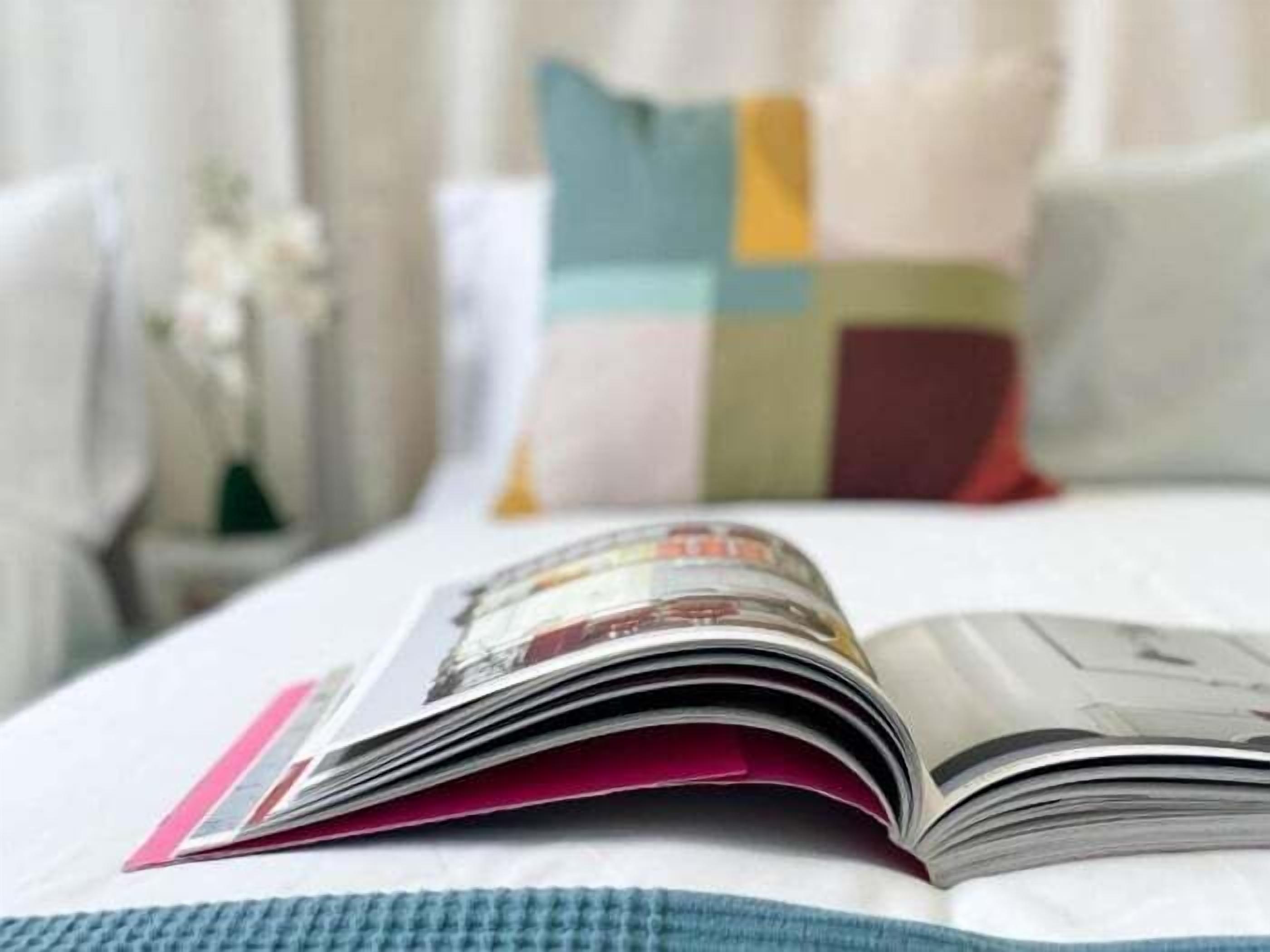 Una cama con una revista, almohadas y una manta azul de punto.