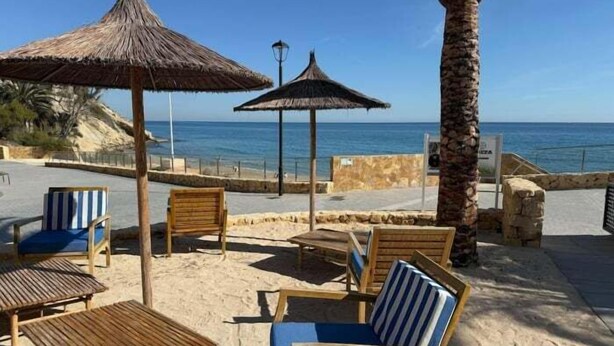 Un espace aménagé avec des chaises et des tables en bois, des parasols en chaume et une vue sur la mer, situé au bord de la plage.