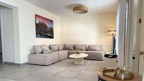 Un salon moderne avec un canapé d’angle, une table basse ronde et un tableau accroché au mur.