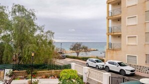 Un immeuble d’habitation doté de balcons, offrant une vue sur la mer et dont les voitures sont garées devant.
