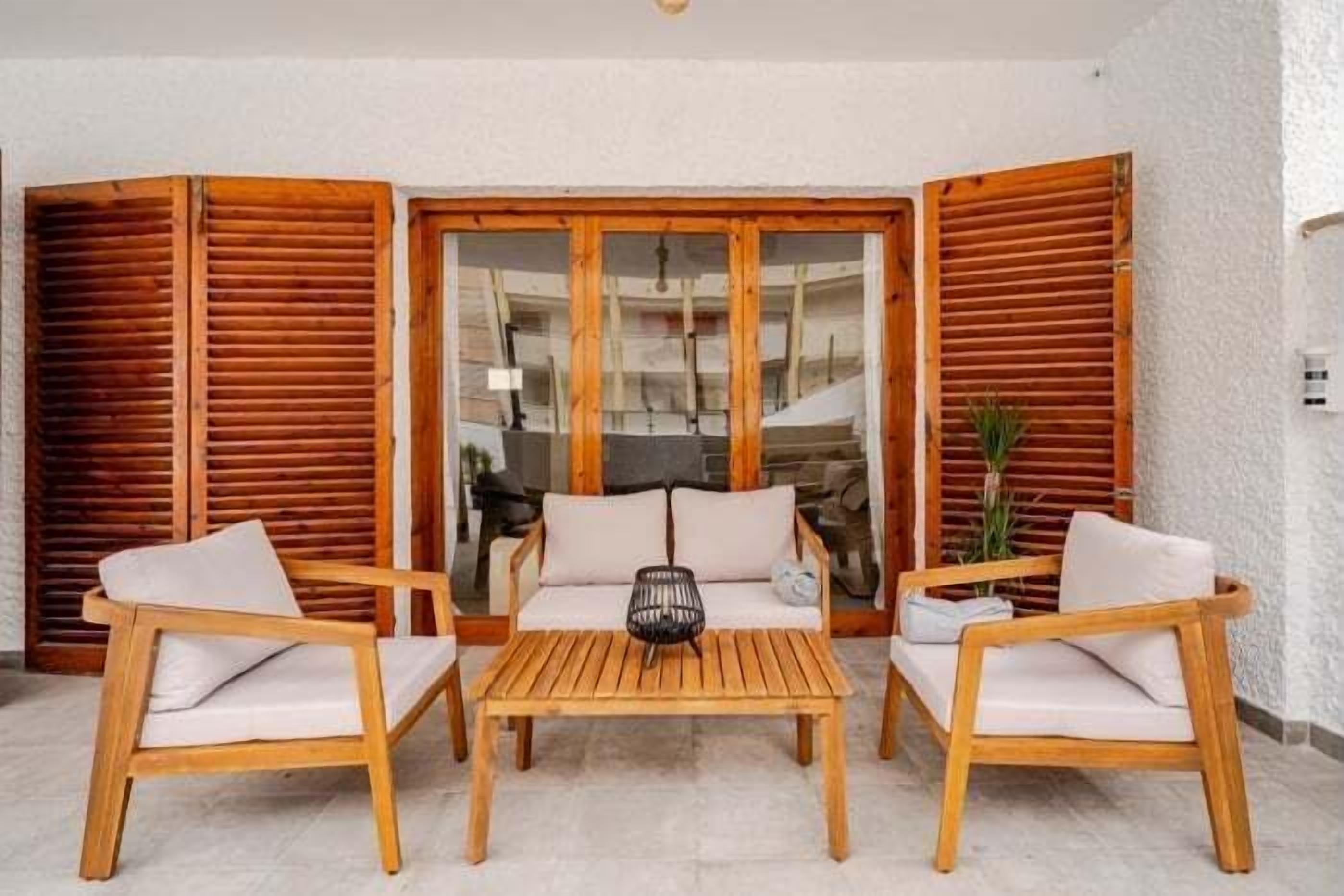 A wooden outdoor seating area with a table and two chairs, a glass door, and a plant.