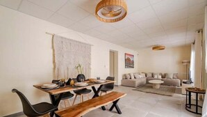Un coin repas avec une table en bois, des chaises noires et un banc. Le salon comprend un canapé et une table basse.