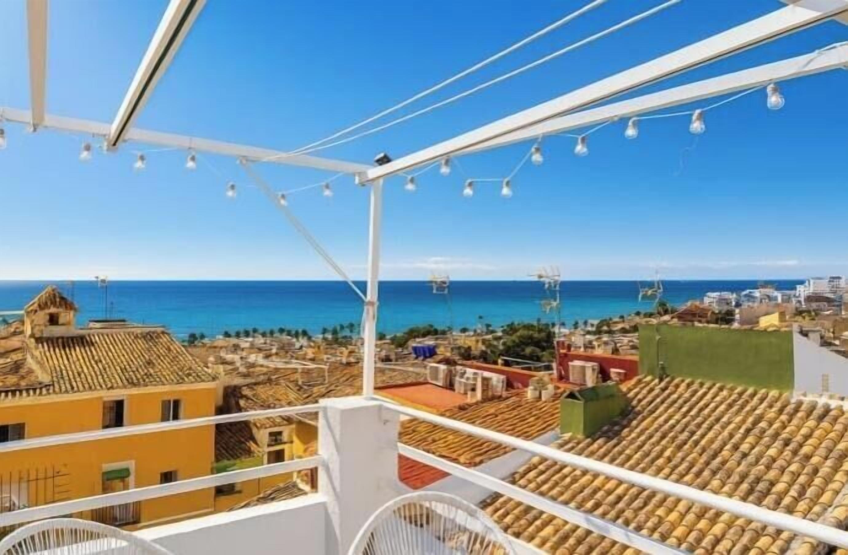 A rooftop terrace with a view of the sea, white railings, and string lights.