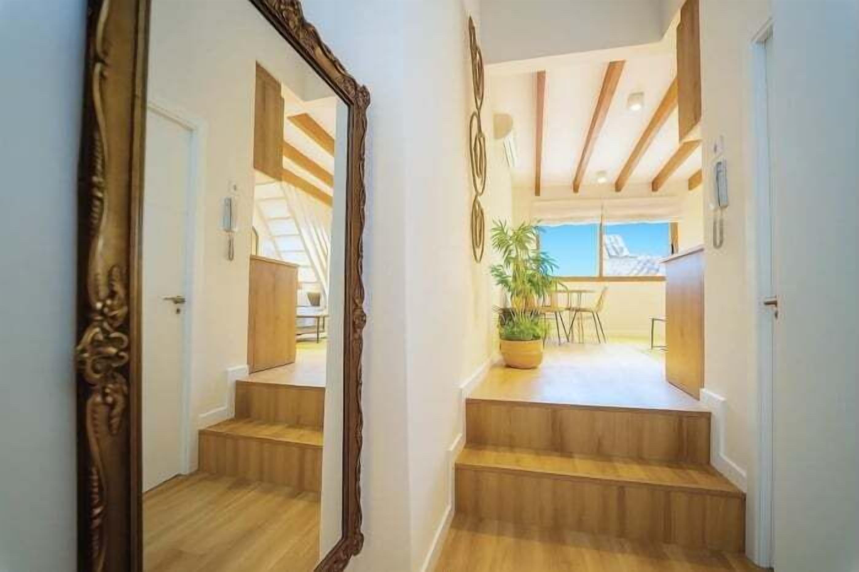Una escalera conduce a un comedor con vistas, un espejo y suelo de madera.