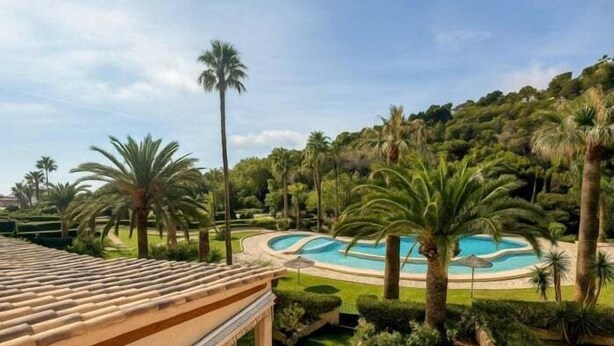 Une piscine entourée de palmiers et de verdure, avec un toit en tuiles visible au premier plan.
