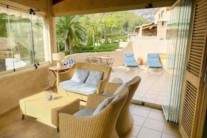 Ein Balkon mit Korbmöbeln, einem Glastisch und Blick auf einen angelegten Garten.