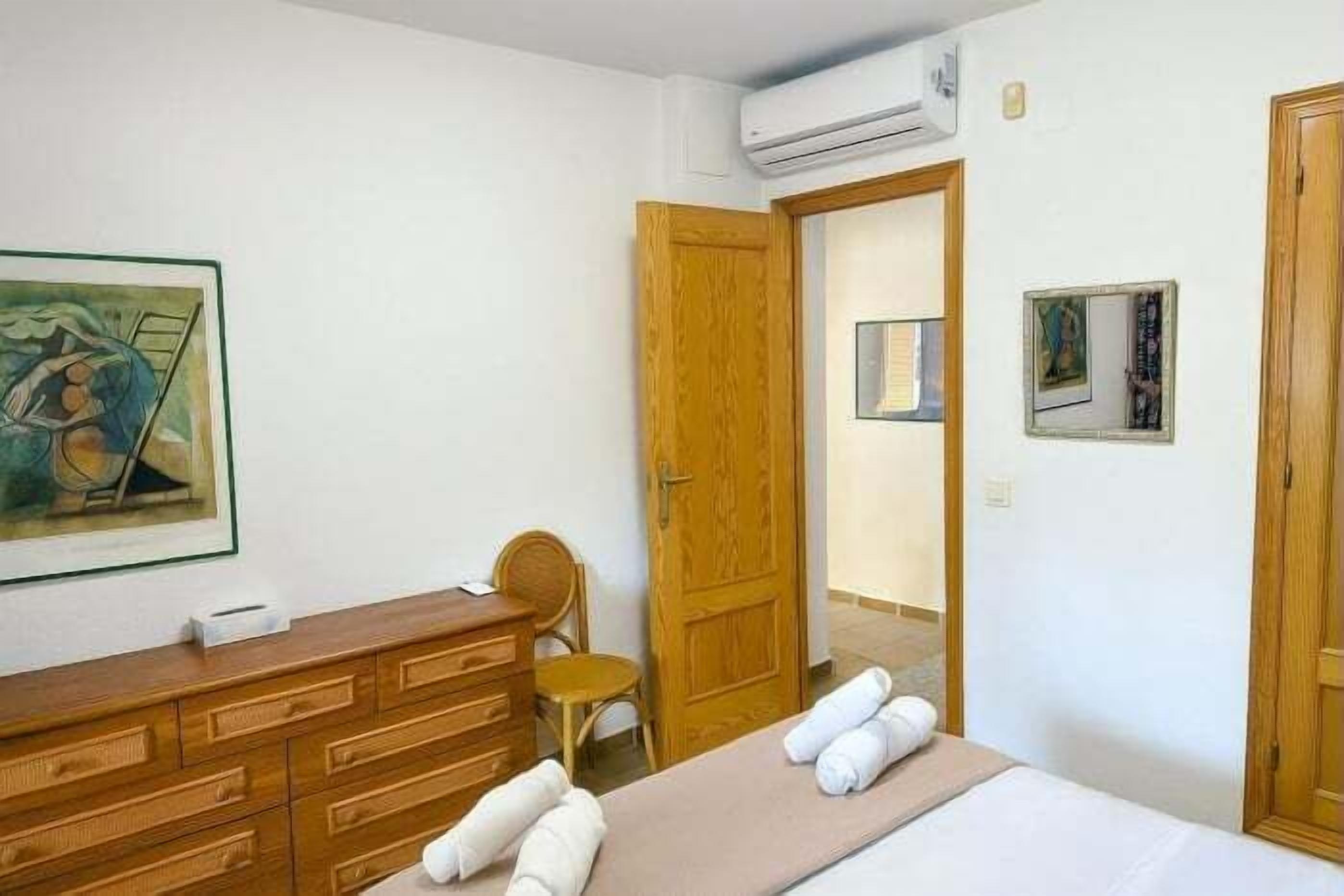 Habitación de hotel con cómoda de madera, cama con toallas, una silla y puerta que da a otra habitación.