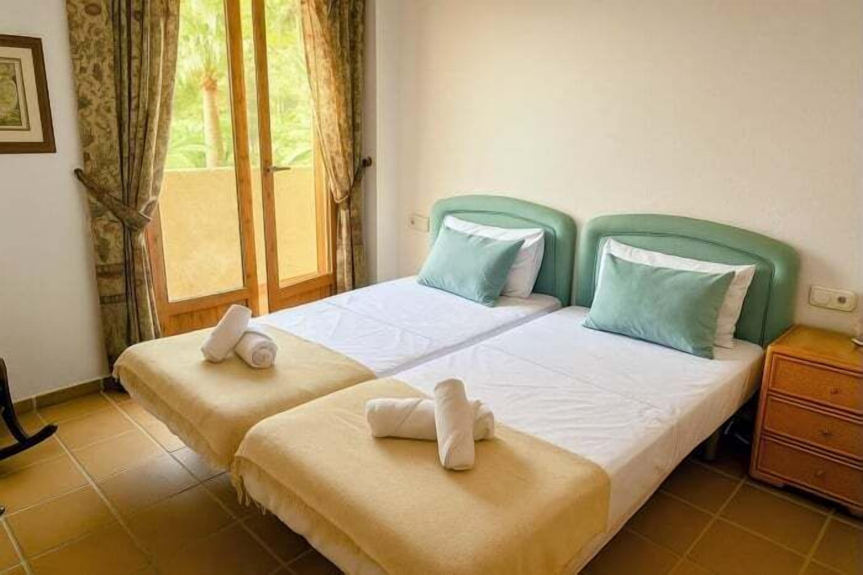 A double bed with two pillows, a wooden nightstand, and a window with curtains.