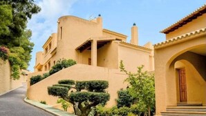 Un immeuble résidentiel à la façade incurvée, doté d’une entrée centrale avec des marches et d’un petit jardin agrémenté d’arbustes taillés et d’un arbre.