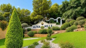 Un espace aménagé, agrémenté d’un panneau indiquant « Altea Hills », entouré d’une végétation bien entretenue et d’un mur de pierres.