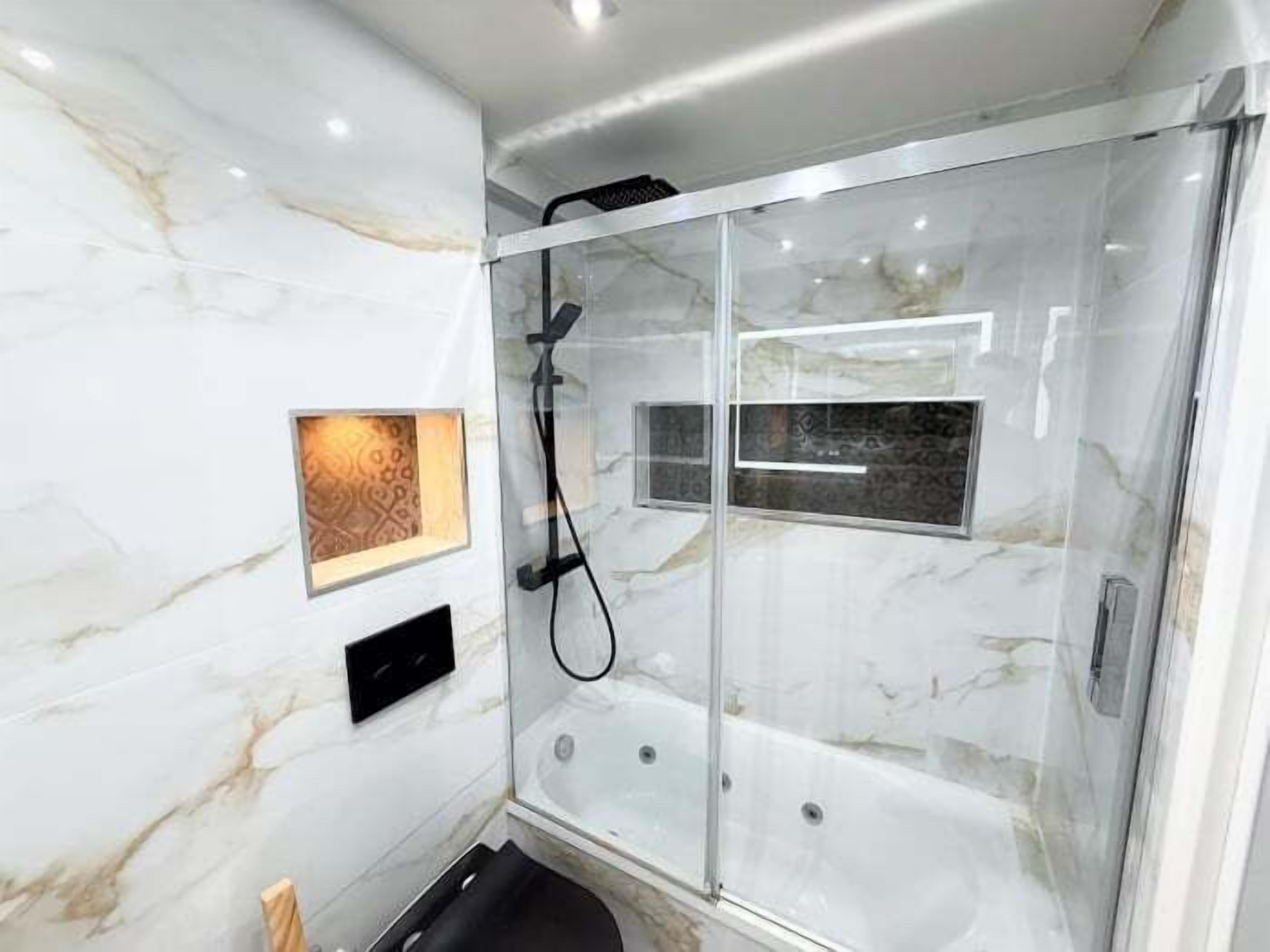 A modern bathroom with a glass-enclosed shower, marble walls, and a small decorative panel.