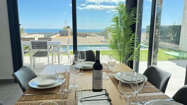 A dining table set with plates, glasses, and a bottle, overlooking a pool and greenery. - Beautiful villa with private pool and sea views (Polop)
