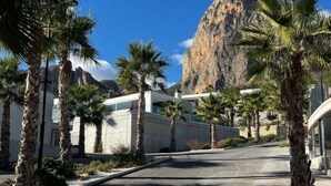 A modern building with a curved facade, palm trees, and a mountain in the background. - Beautiful villa with private pool and sea views (Polop)