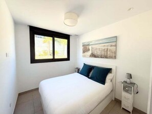 Ein Schlafzimmer mit Bett, Nachttisch, Lampe, Fenster und einem Gemälde an der Wand.