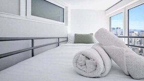 Une chambre d’hôtel avec un lit, une fenêtre donnant sur la ville et une serviette pliée posée sur le lit.