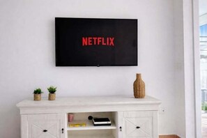A television mounted on a wall with the Netflix logo, a white cabinet below with a vase and two small plants, and a door with a keyhole. - Renovated central apartment with garage and pool (Benidorm)