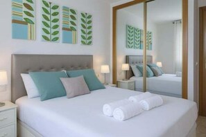 A hotel room with a bed, pillows, a nightstand, a mirror, and artwork on the wall. - Apartment with Summer and Winter Pools (Benidorm)