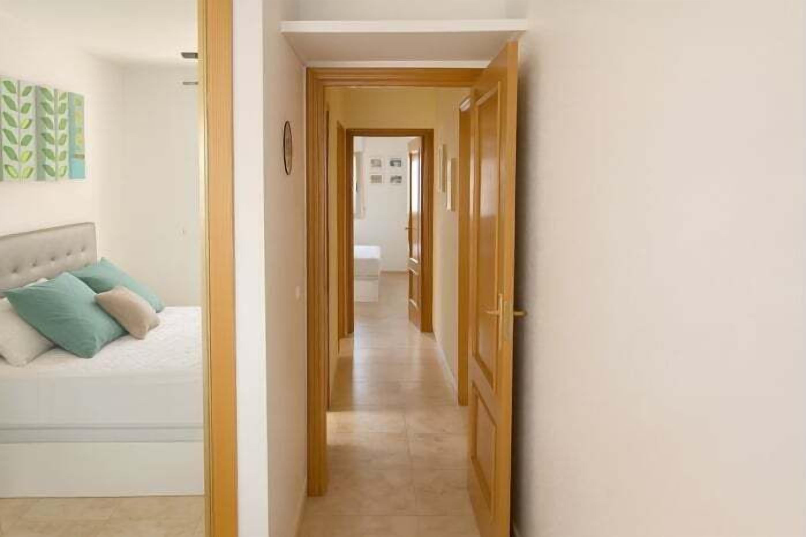 A hallway leading to a bedroom with a bed and a nightstand.