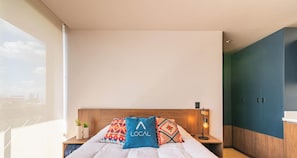 A modern hotel room with a large bed, a nightstand with a lamp, a view of the city, and a wardrobe. - Loft with kitchenette, balcony and access to gym and coworking space (Ciudad de México)