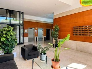 A modern lobby with a black sofa, potted plants, a reception desk, and an elevator. - Apartment with Sea Views and Covered Parking (Benidorm)