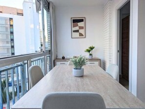 Ein moderner Essbereich mit einem langen Tisch, Stühlen, einer Topfpflanze und einem gerahmten abstrakten Gemälde an der Wand.