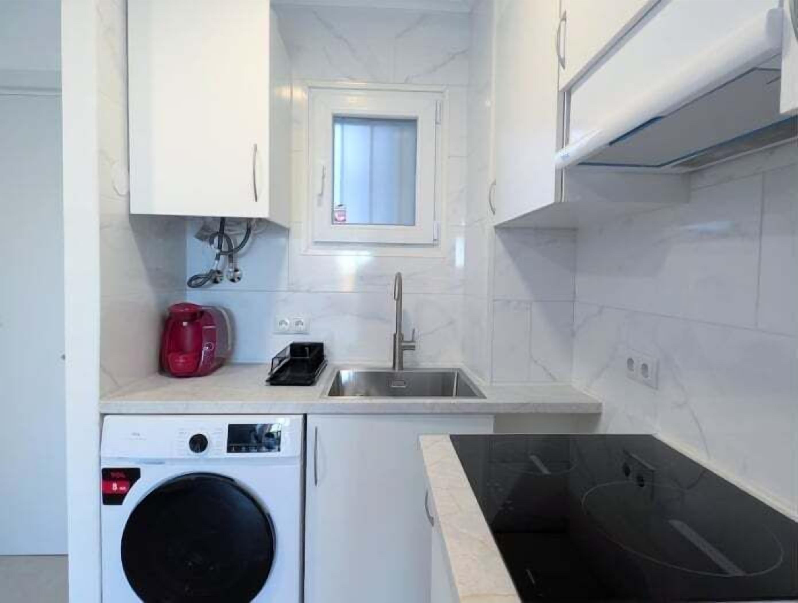A compact kitchen with a washing machine, a sink, and a window.