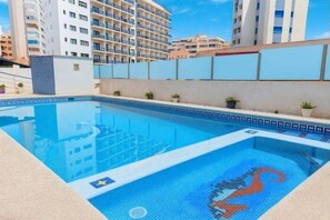 Ein Schwimmbecken mit blauem Mosaikdesign, umgeben von einer niedrigen Mauer und Pflanzgefäßen.