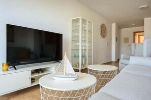 Ein modernes Wohnzimmer mit Flachbildfernseher, einer Glastruhe, einem runden Couchtisch und einem weißen Sofa.