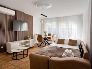 Ein modernes Hotelzimmer mit einem Bett, einem Fernseher, einer Essecke und einem großen Fenster.