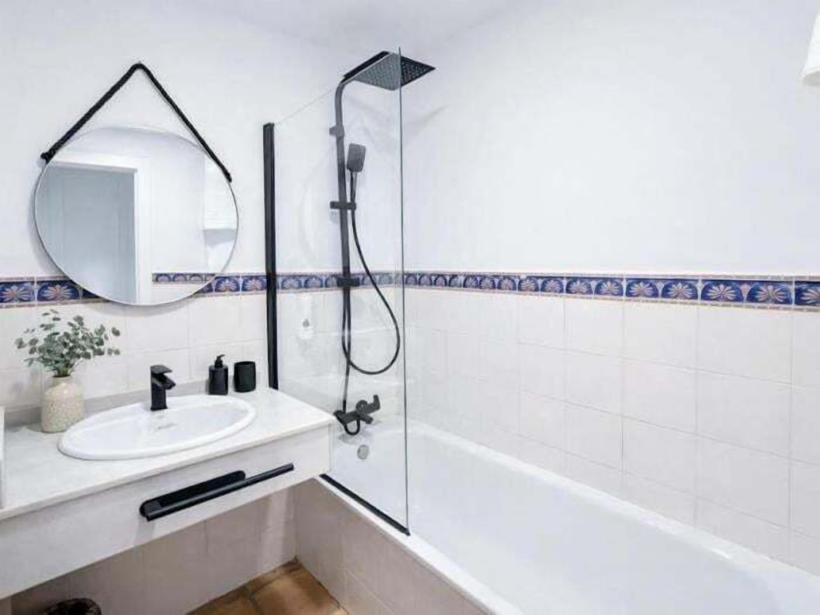 A bathroom with a white sink, a mirror, a shower, and a tiled wall.